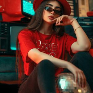 Trendy woman in red attire poses indoors with retro TV and disco ball, exuding a cool and modern vibe.
